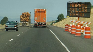 Reader board sign and orange barrels on the highway right of way warn motorists of upcoming work zone on I-5.