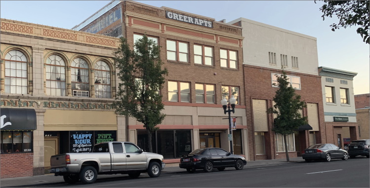 Cars parked in front of mixed-use building with “Greet Apts” sign displayed at the top