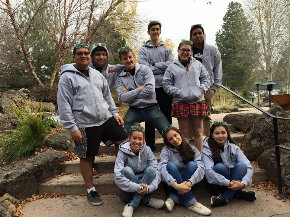 Nine Teen Advisory Board members sit outside, smiling and wearing matching gray sweatshirts