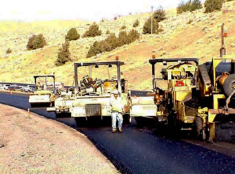 Construction machines on a newly paved road with a person standing in the middle of the road