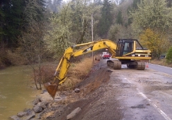 An excavator works to repair and shore up a roadside that has eroded.