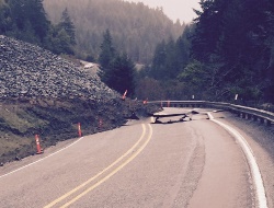 Landslide covers entire left lane of a two-lane road. The right hand lane is left badly damaged. 