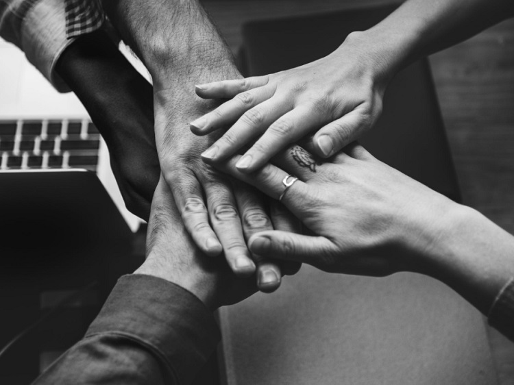 Monochrome photo of 5 hands coming together in team work