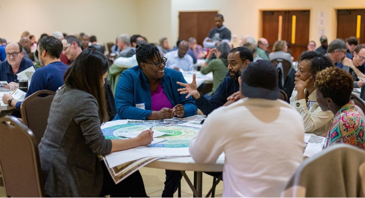 People sitting and conversing around tables with maps and figures out in front of them