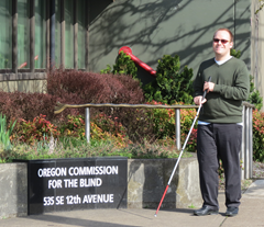 Man with white cane stands in front of OCB main office.