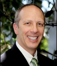 Arnold, light brown hair wearing a black suite jacket, white shirt and a green tie.
