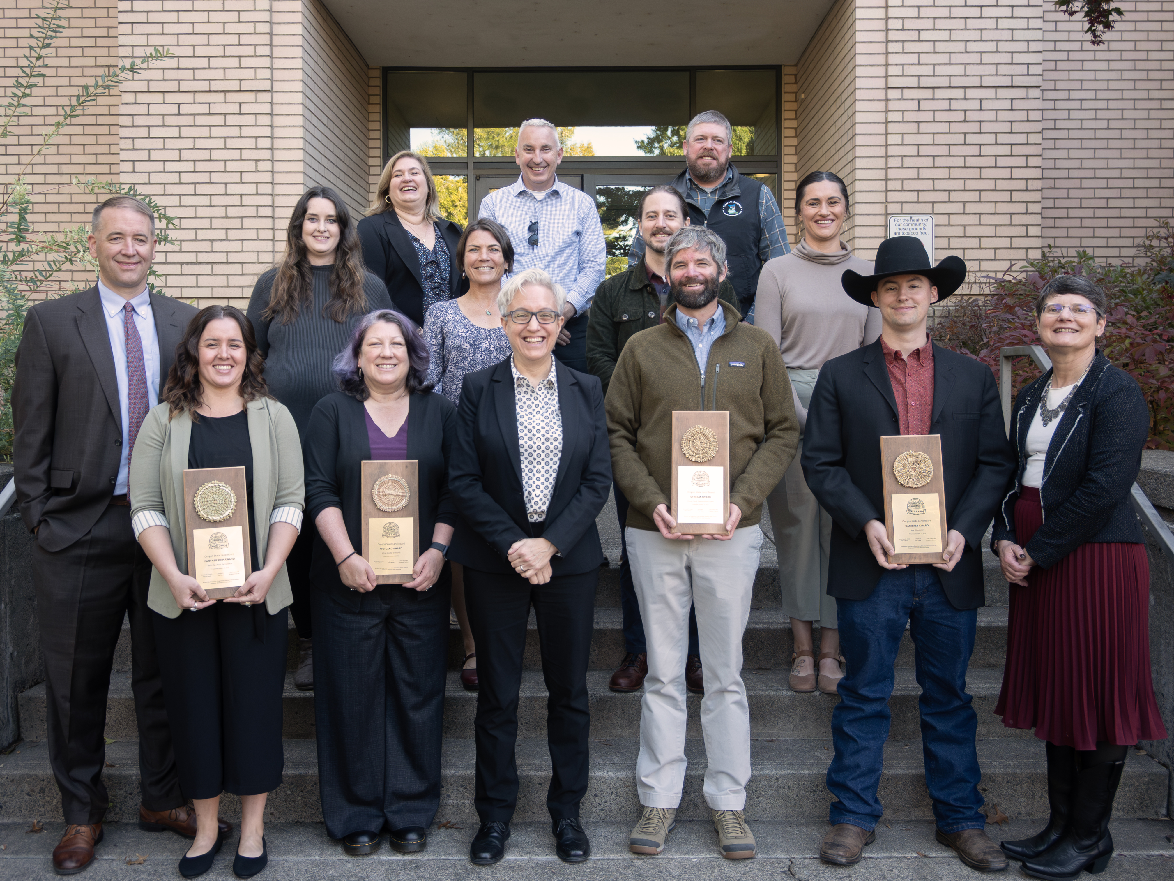 Group of people stand outside behind three people holding awards.
