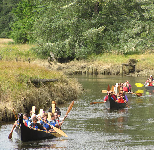 People paddle down river in canoes.