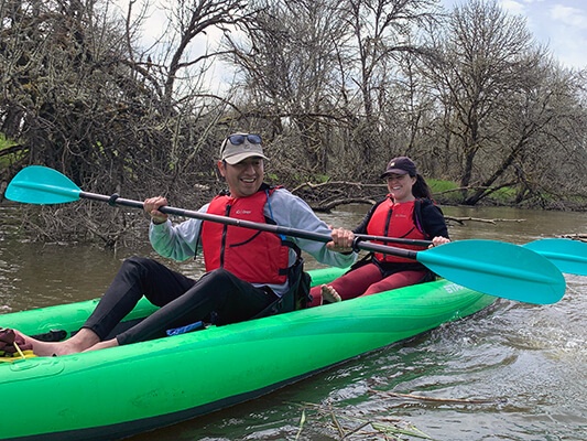 Two people holding paddles in a green kayak on a river.