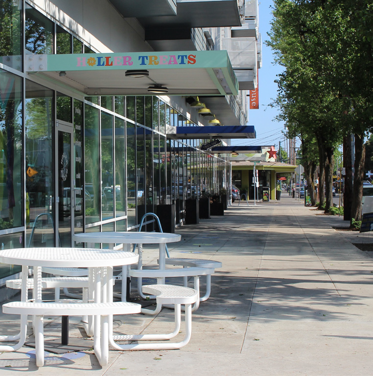 A wide sidewalk with tables and benches for storefront customers.