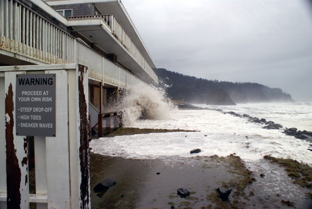 Sideview of a three-story beach property. Waves crash against the first floor of the structure.