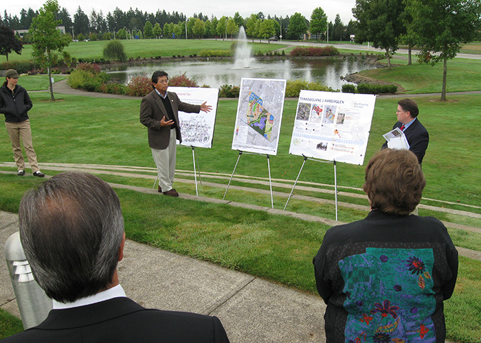 Men present maps outdoors in a public planning meeting
