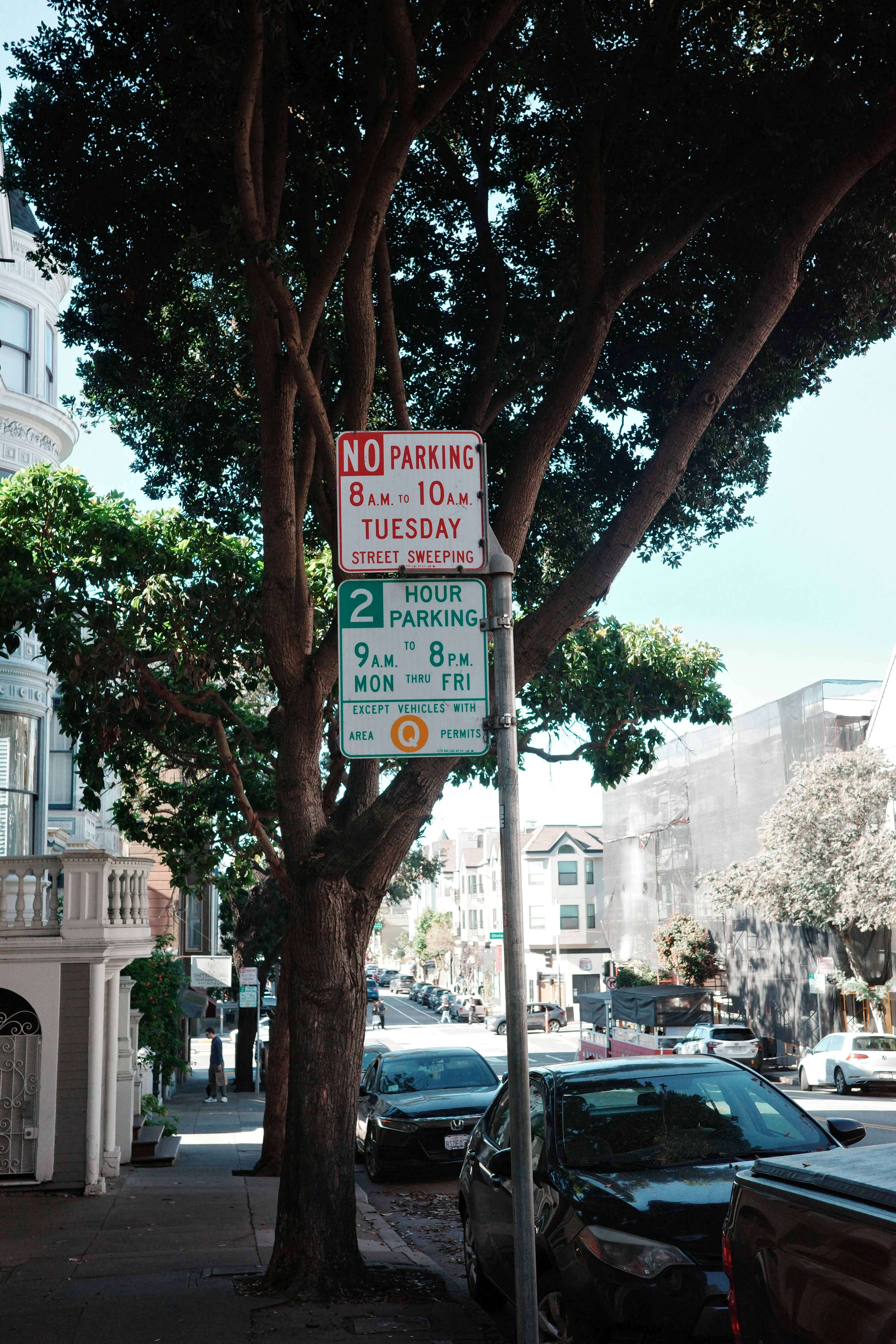 A red "no parking" and green "2 hour parking" signs  specify when cars can park next to the sidewalk.
