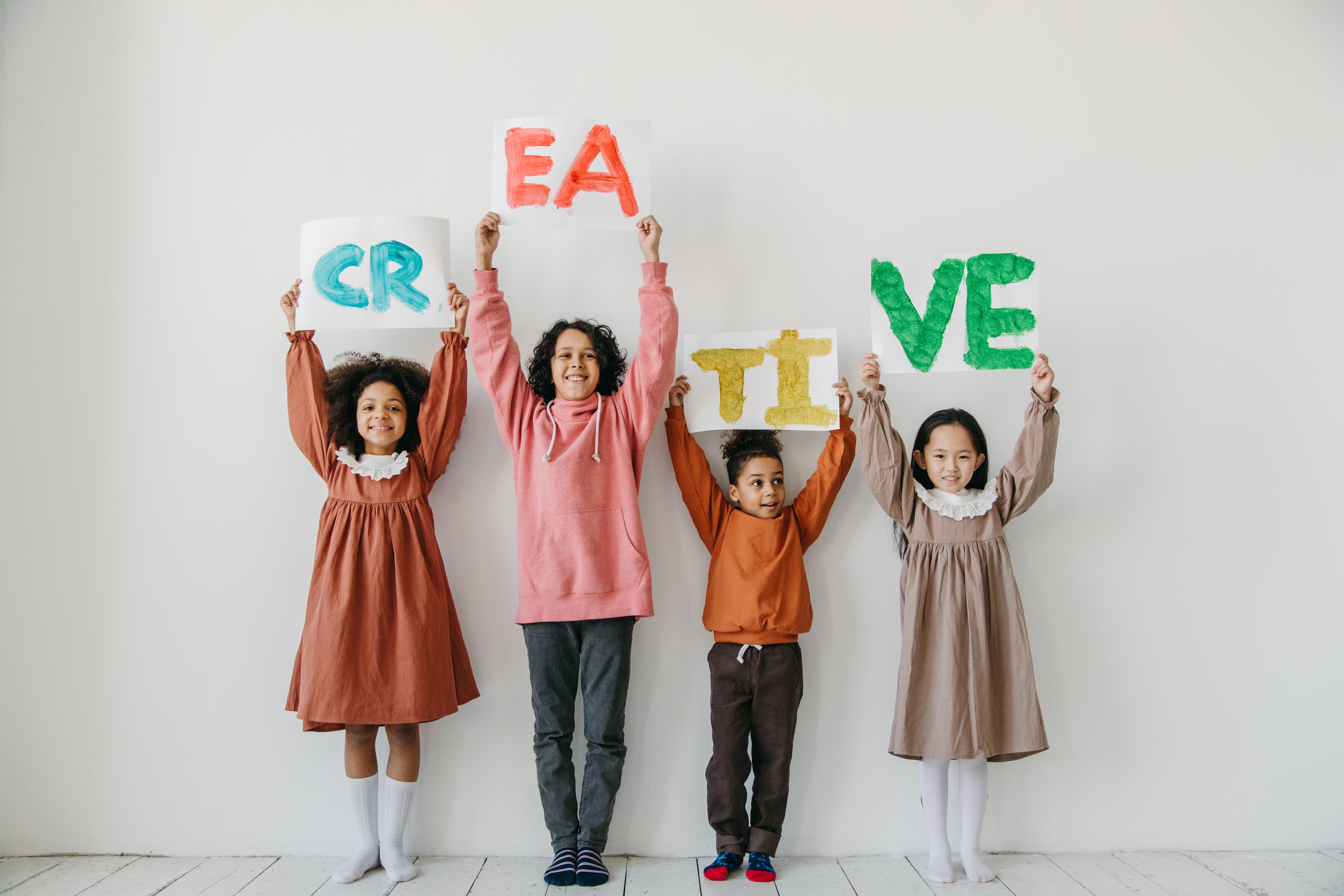Four children hold up painted signs spelling the word 'creative'