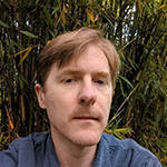Photo of Adam, a man with short light brown hair combed toward the right and a short mustache. 
