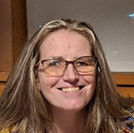 Photo of Danica, a woman with long blonde hair and gold rimmed glasses while smiling at the camera. 