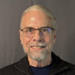 Photo of Daniel, a man with short grey hair combed toward the left and a short mustache and beard. 