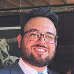 Photo of Julian, a man with short black hair combed toward the left and a short mustache and beard. 