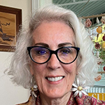 Photo of Kathy, a woman with shoulder length white hair. She is looking and smiling at the camera. She is wearing a red shirt.