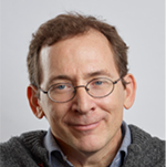 Photo of Randall, a man with short red hair and thin rimmed glasses. He is wearing a grey sweater over a blue, button-up, collar