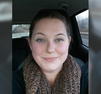Kim, a woman with shoulder length blonde hair smiling at the camera. The background is a brick wall.
