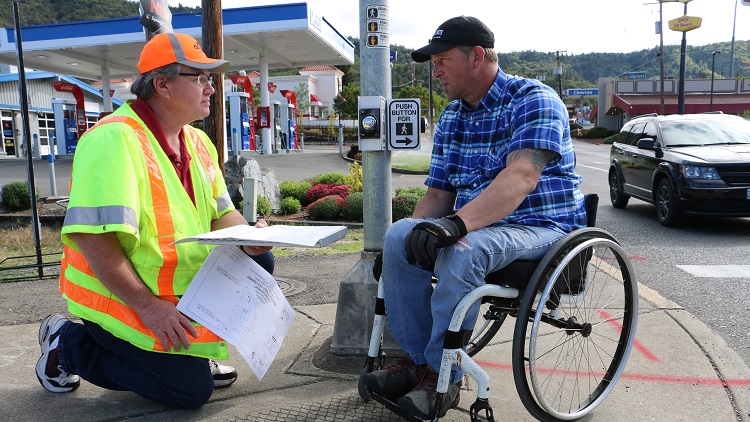 ODOT staff in safety vest addressing concerns from person in a wheel chair near the curb ramp.