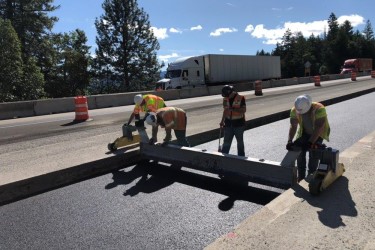 Highway construction employees smoothing fresh pavement.