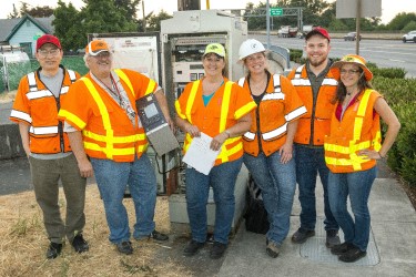 Group of traffic employees standing outside in front of a big electrical box and smiling at the camera