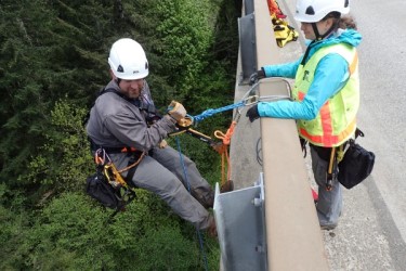 Employee beginning to repel down the side of a bridge in a harness