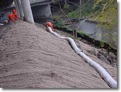 Workers place an erosion control strip under a bridge during construction activities.