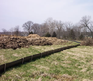 a grassy hill with an erosion control fence in the middle of it on the downward slope. A thin, black fence about three feet high