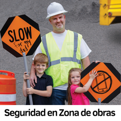 Un señalizador de zonas de obras abraza a 2 niños que levantan señales que dicen: Lento para mi papá y no celulares.