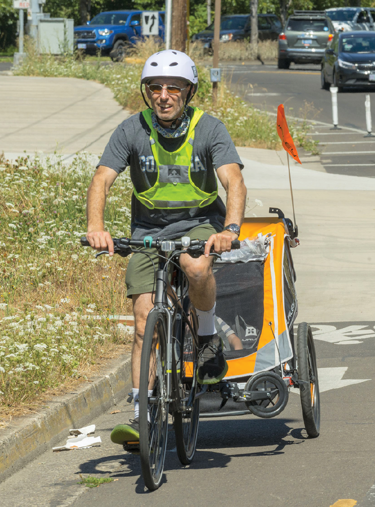 Image - a man wearing a reflective vest riding a bicycle with a passenger trailer