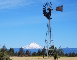 A windmill faces north with a view of Mt. Hood to the east against blue skies