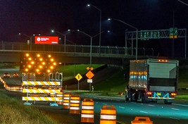 Highway at night with construction barrels and illuminated arrow board closing a travel lane.