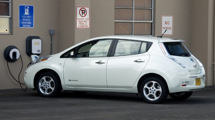 White Nissan Leaf electric car plugged into a charger next to a public building