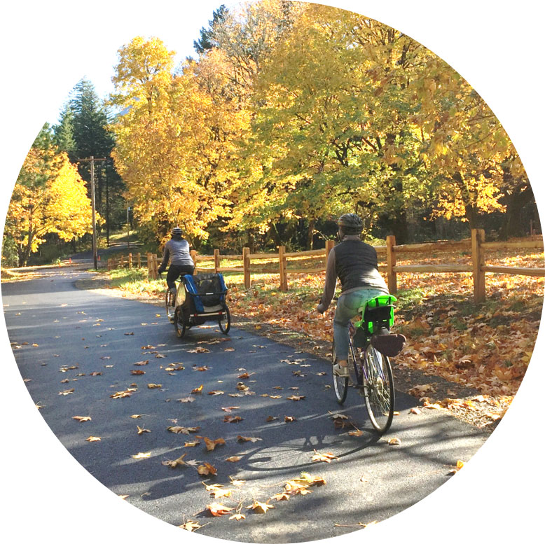 Two people riding bikes single file along a multiuse path