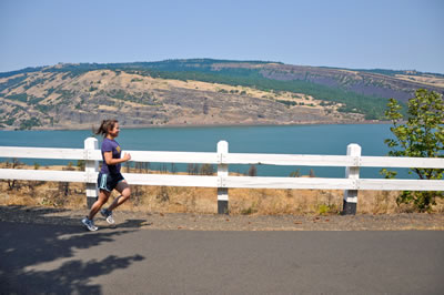 Girl jogging next to the iconic white fence with view of the Columbia River in the back.
