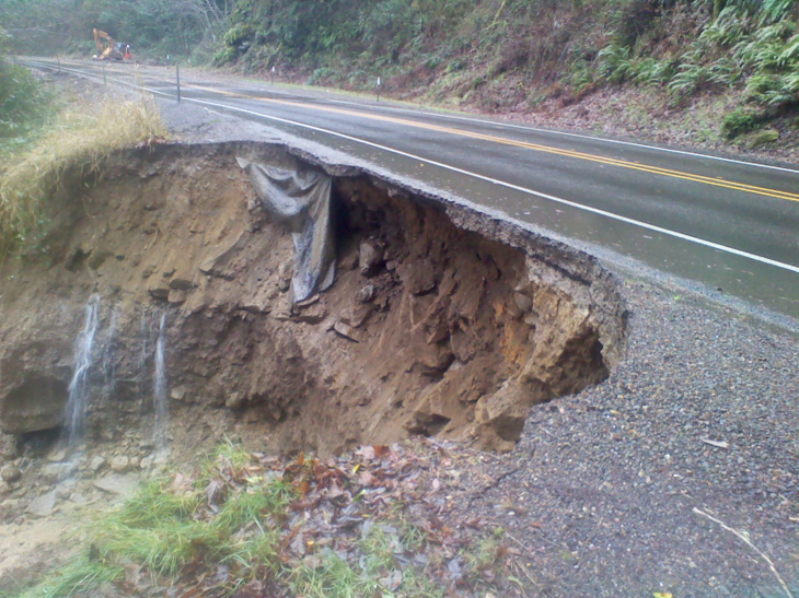 An image showing the need for a culvert: Water coming out of the earth under an Oregon road with erosion underneath the road.