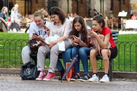 Teens sitting on a park bench, looking at their phones