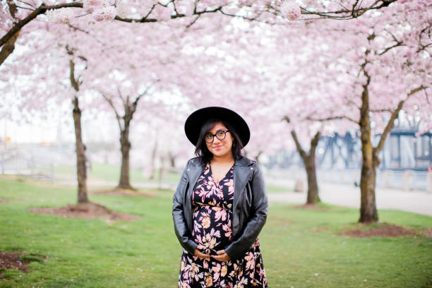 Pregnant Hispanic Woman Portrait Portrait of a pregnant hispanic woman in her mid 20s. She is wearing a maternity dress and standing in a park in Portland Oregon full of blooming cherry blossoms in the spring time. portland oregon people stock pictures, royalty-free photos & images