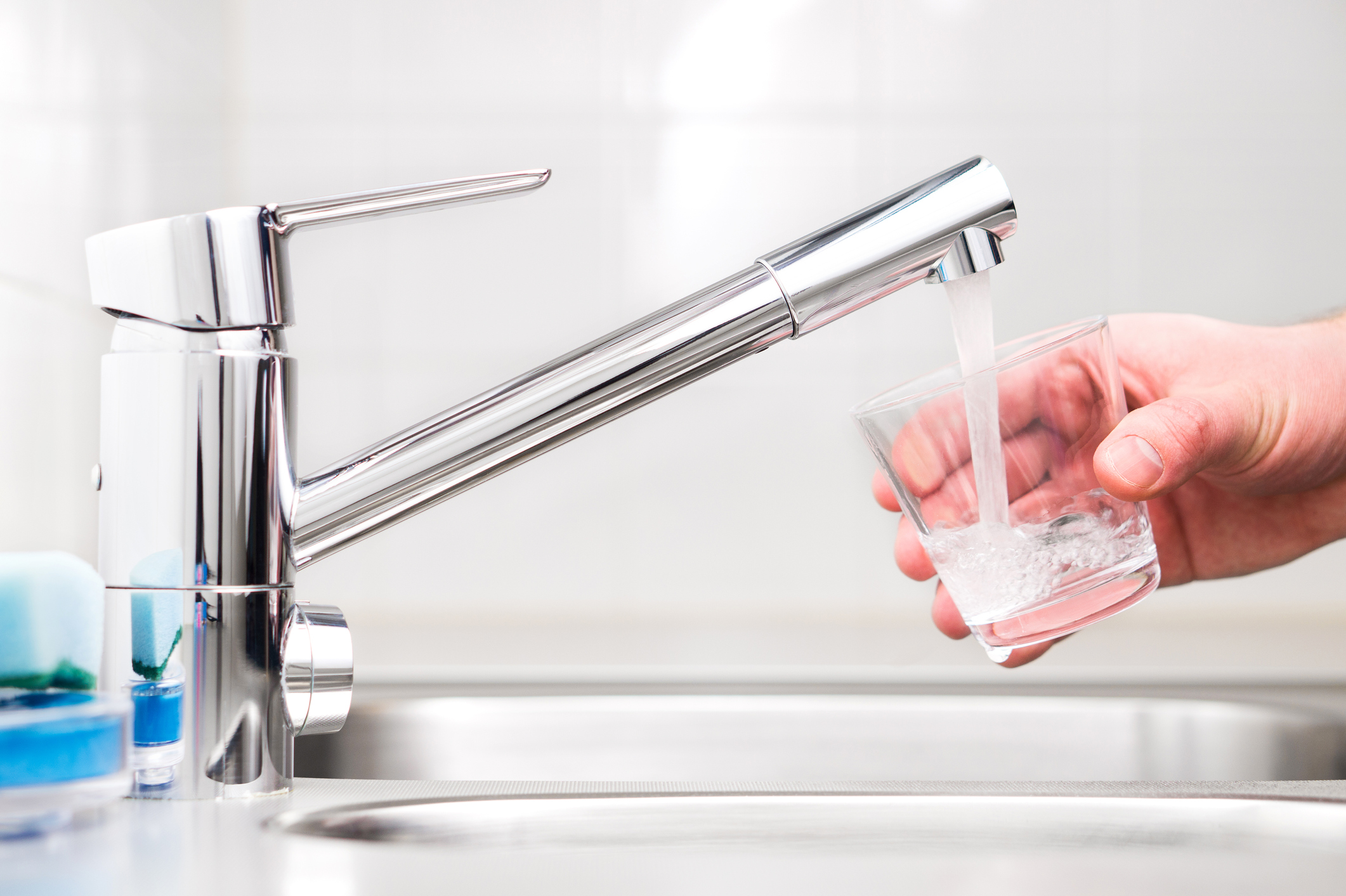 A hand holding a clear water glass under a running sink faucet