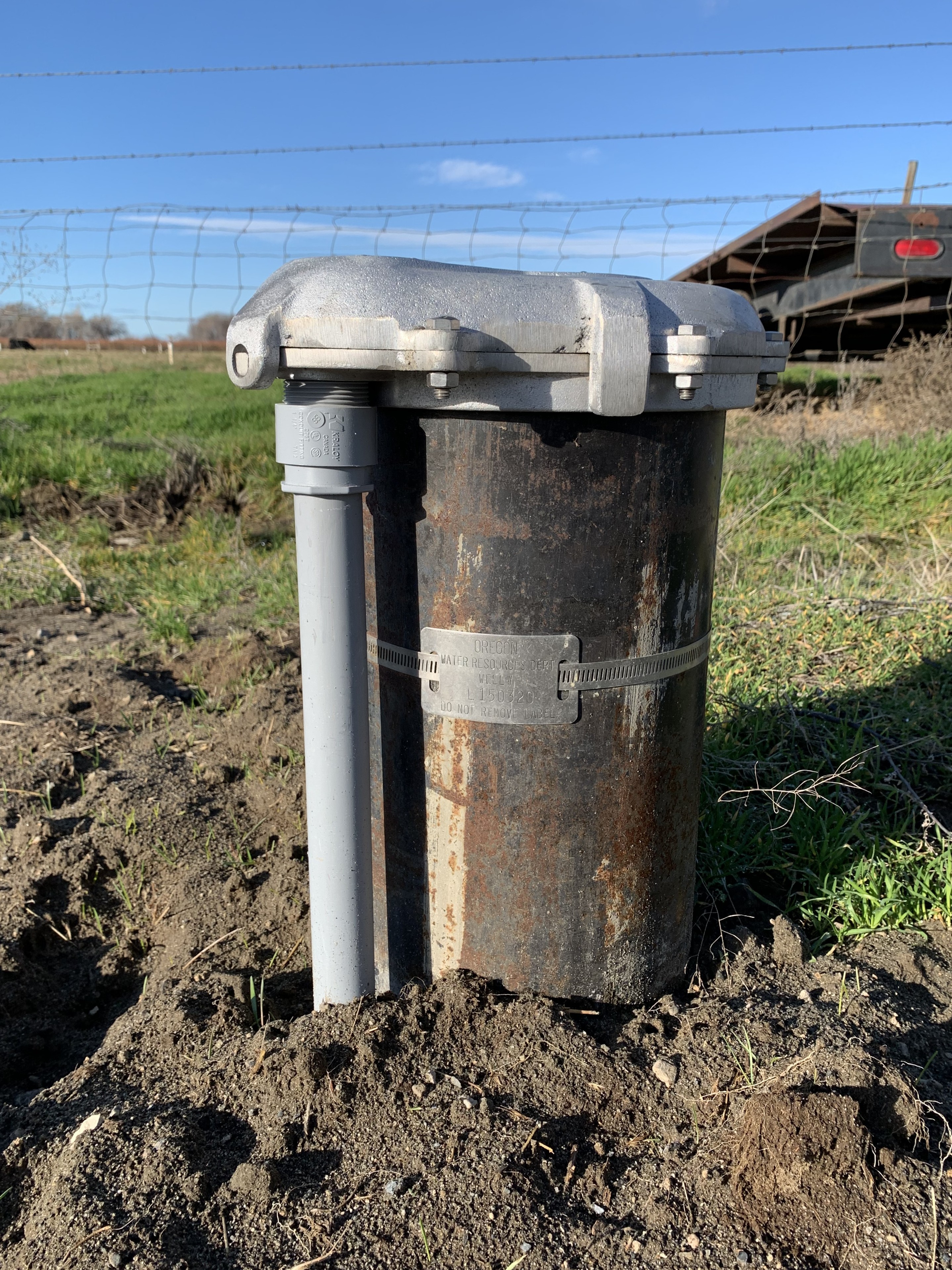 A wellhead with a fence and green field behind it.