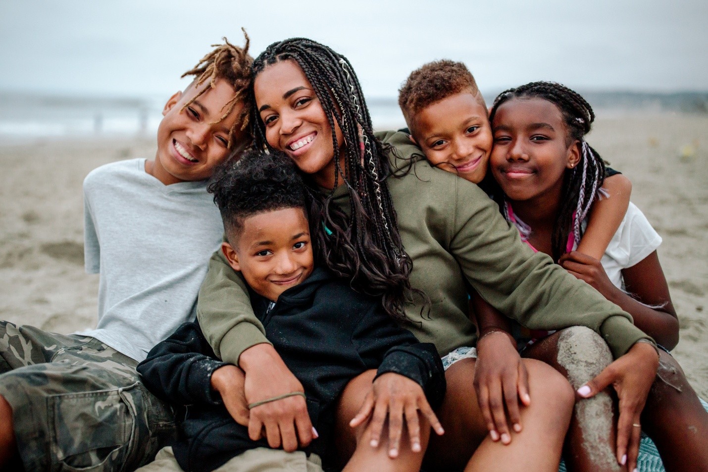 A parent with 4 kids together on the beach.