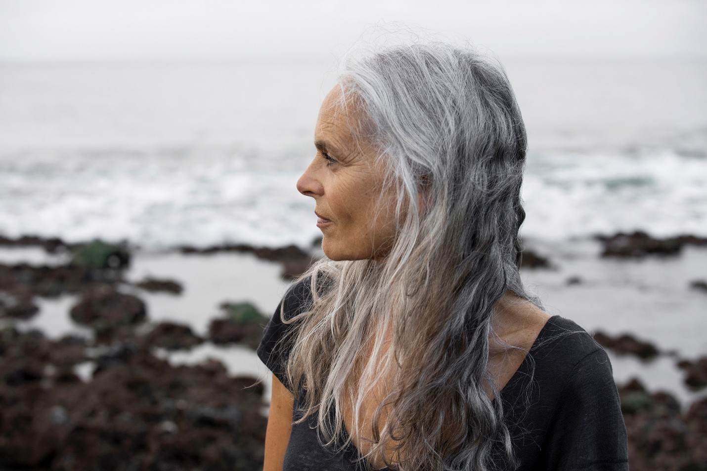 The profile of a person with long grey hair. The ocean is behind them.