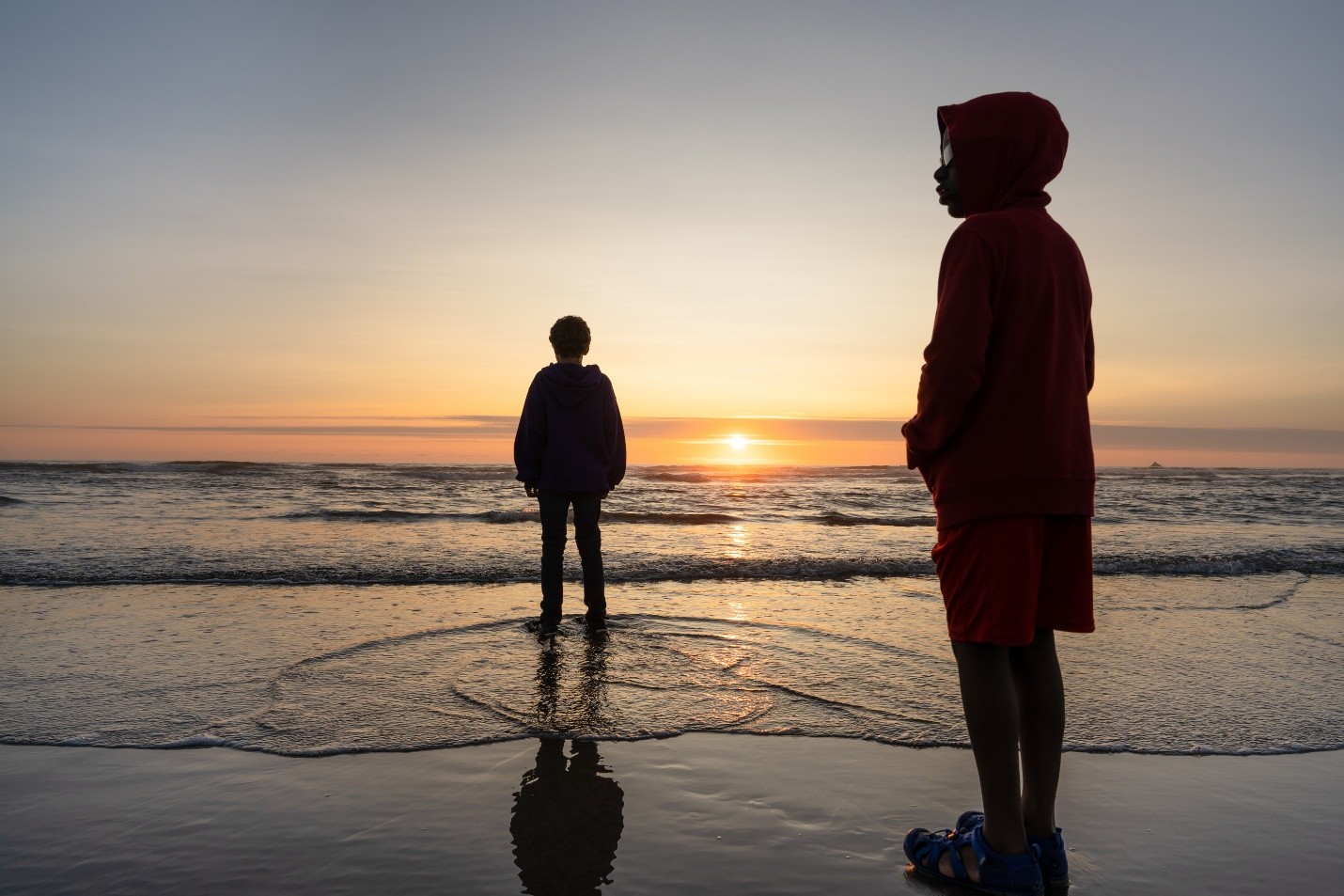 2 kids standing near the ocean during a sunset.