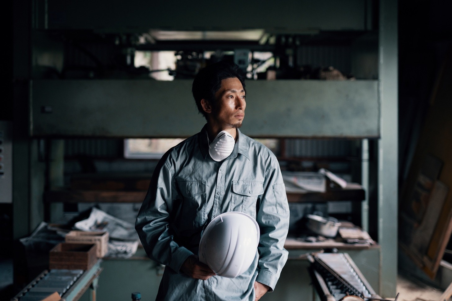A worker holding a white hard hat with a white mask around their neck.