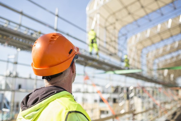 A construction worker wearing an orange hard hat looking out at a construction site.