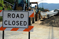 Bulldozer and other heavy equipment working behind large ROAD CLOSED sign