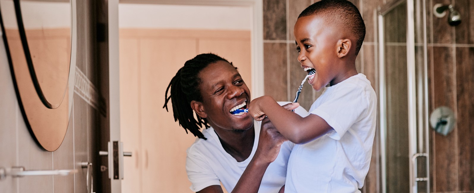 Photo of adult man brushing teeth with child in a bathroom.